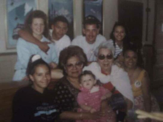 A large family smiles and holds a baby, enjoying quality time in a lively indoor space.