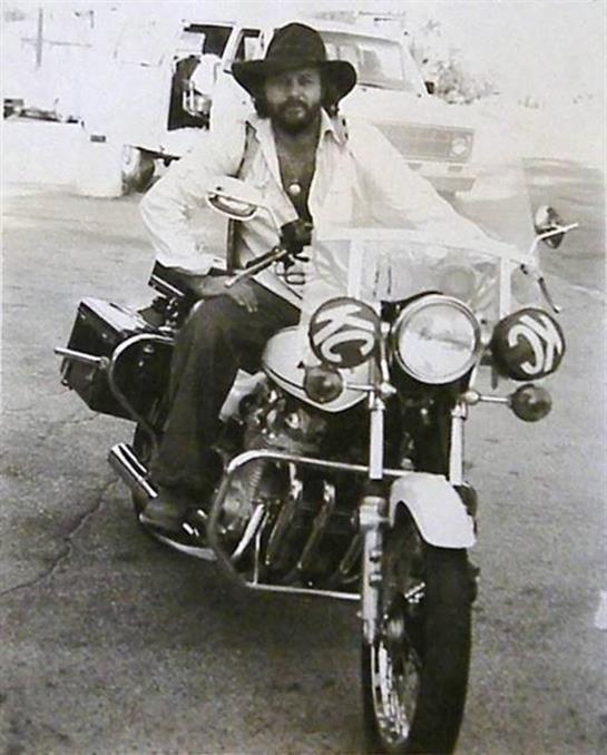 A man in vintage attire rides a motorcycle, enjoying a carefree day outdoors.