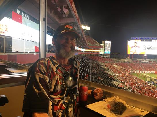 A man sits in a luxury stadium box, enjoying food and drink while watching the game.