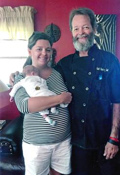 A couple smiles proudly while holding their newborn at a cozy home gathering with friends.