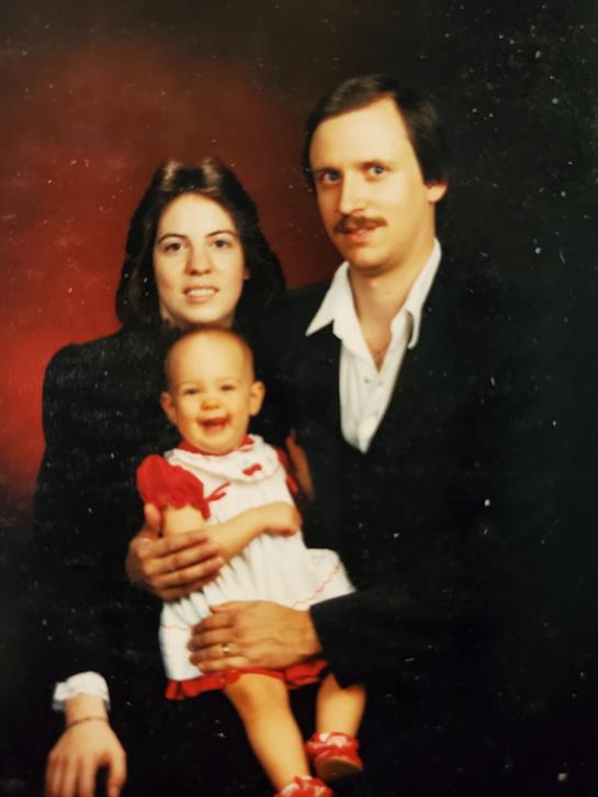 Parents hold their happy child in a close embrace against a dark background, displaying warmth.