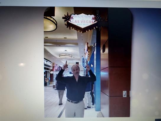 Individual stands under a vibrant sign, celebrating, with shoppers in the background.