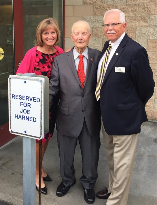 Three people stand together smiling in front of a reserved sign for Joe Harned.