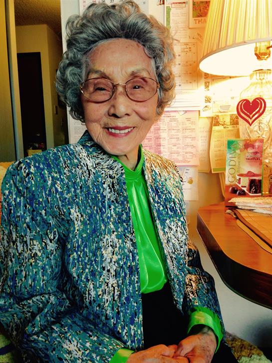 An elderly woman with a warm smile enjoys her time at a well-organized desk with colorful decor.