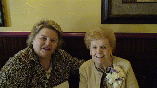 Two smiling elderly women share a joyful moment at a family gathering in a restaurant setting.