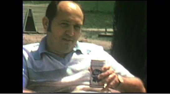 A man sits comfortably outdoors, holding a drink, enjoying a relaxed moment in the sunshine.