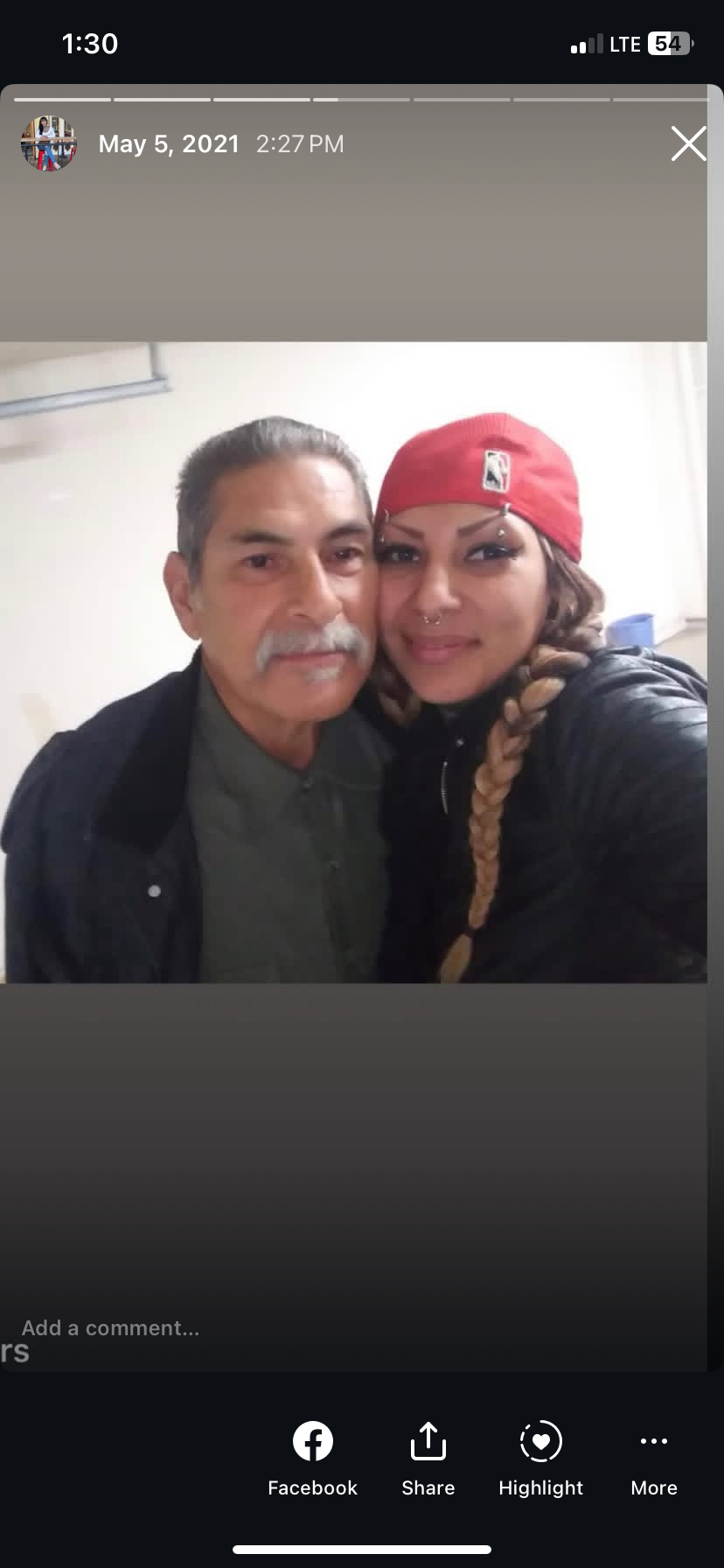 A man and a woman share a warm embrace, smiling with joy in a simple indoor setting.