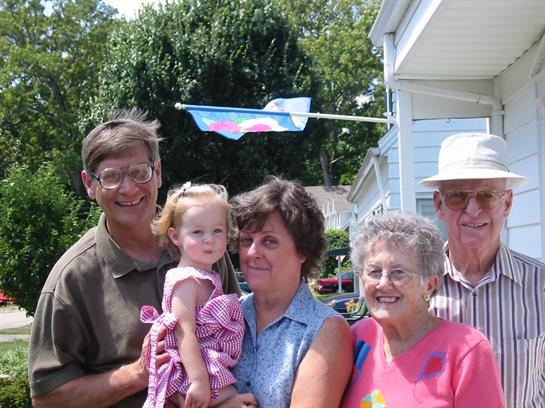 A joyful family gathering takes place outdoors with adults and children smiling at the camera.