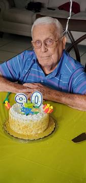 A man proudly smiles at his colorful cake celebrating his 90th birthday.