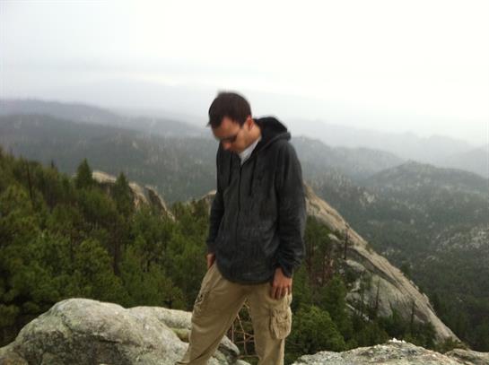 A hiker stands on rocky terrain, gazing down at the valley shrouded in mist and trees.