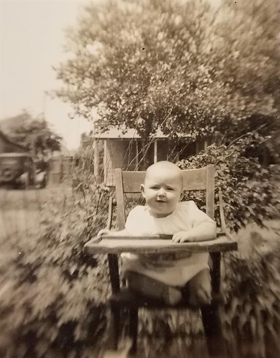 A baby enjoys playtime in a garden, seated in a wooden chair surrounded by greenery.