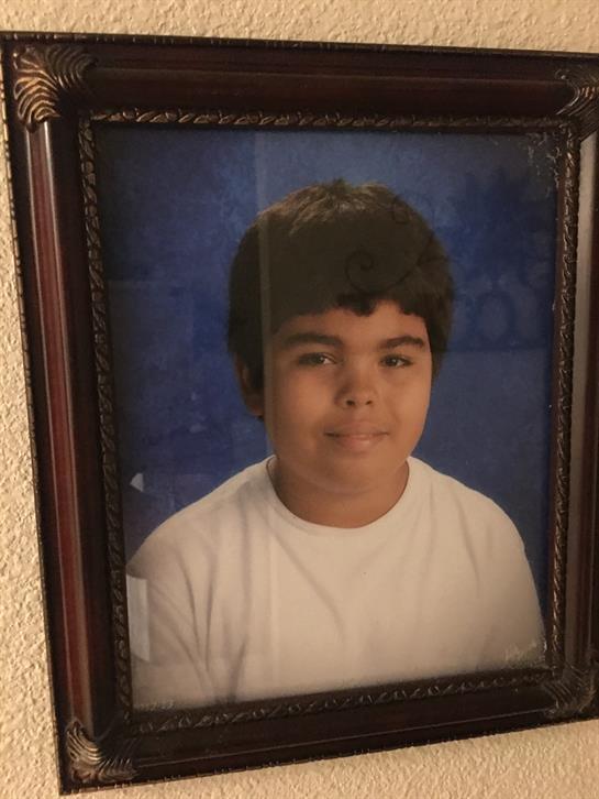 A boy in a white shirt smiles confidently for his school portrait with a blue background.