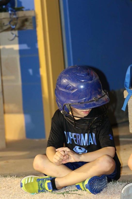 A young player in a helmet sits quietly on the bench, deep in thought during practice.