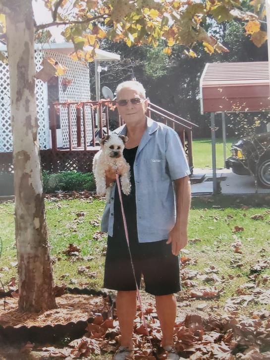 Woman stands in backyard holding small dog, enjoying a sunny afternoon with greenery around.
