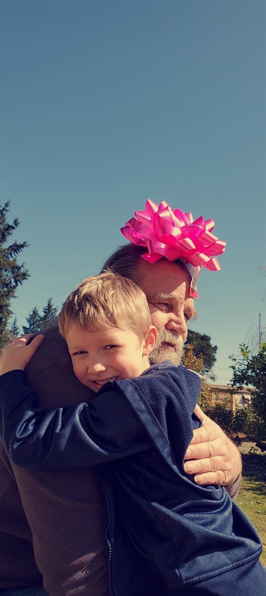 A joyful boy hugs an older man in a pink bow, surrounded by greenery.