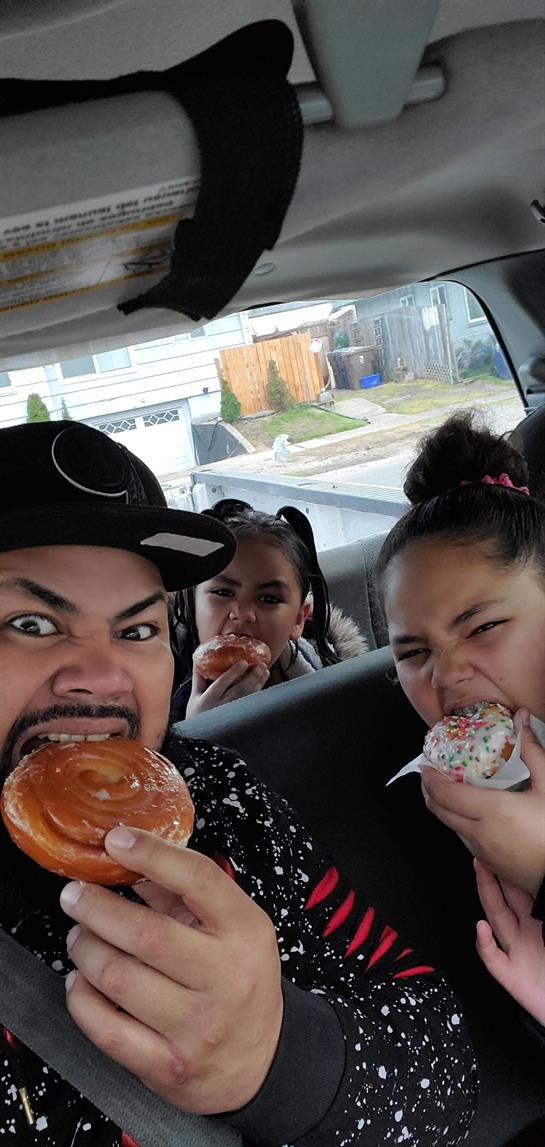 Three smiling individuals savoring sweet pastries with excitement inside a car.