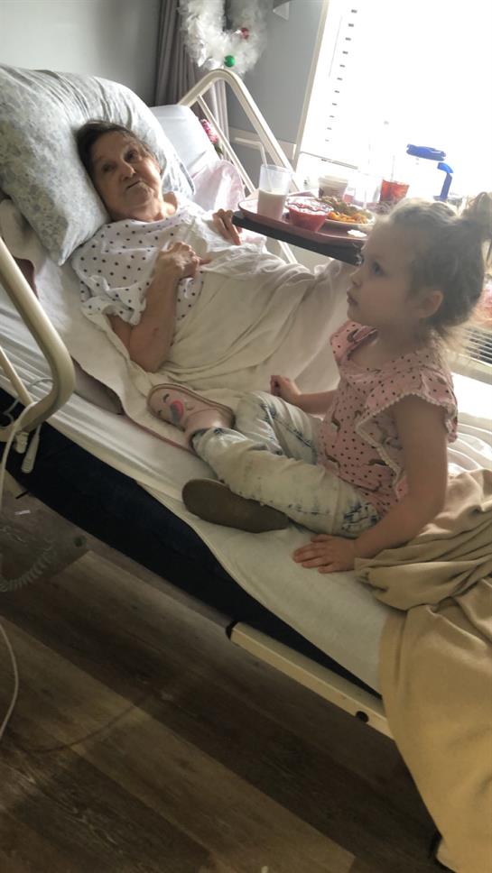 A young girl sits on a hospital bed, engaging with a patient during a visit, offering comfort.
