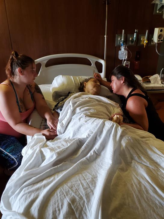 Two women sit by a hospital bed, providing comfort and support to a family member in need.
