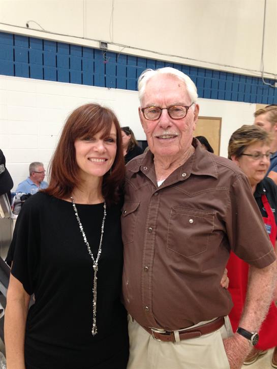 A woman and an elderly man smile together during a joyful community event in a hall.