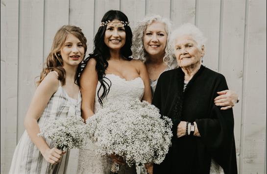 Four women, including a bride, smile happily with flowers in a natural setting.
