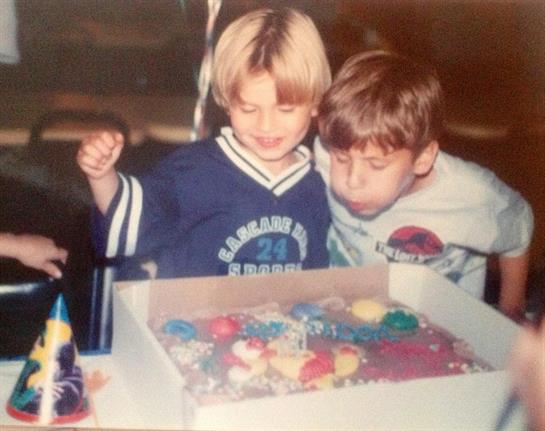 Two children eagerly admire a decorated cake at a festive birthday gathering, smiling broadly.