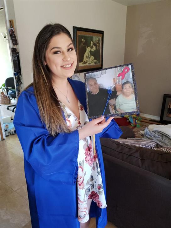 Young graduate proudly holds photo of loved ones while celebrating her special day at home.