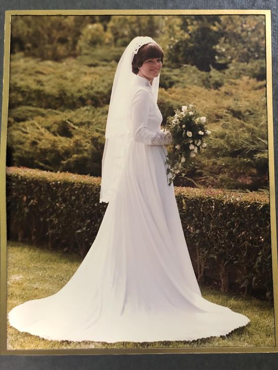 A bride in a white wedding dress holds a bouquet in a floral garden.
