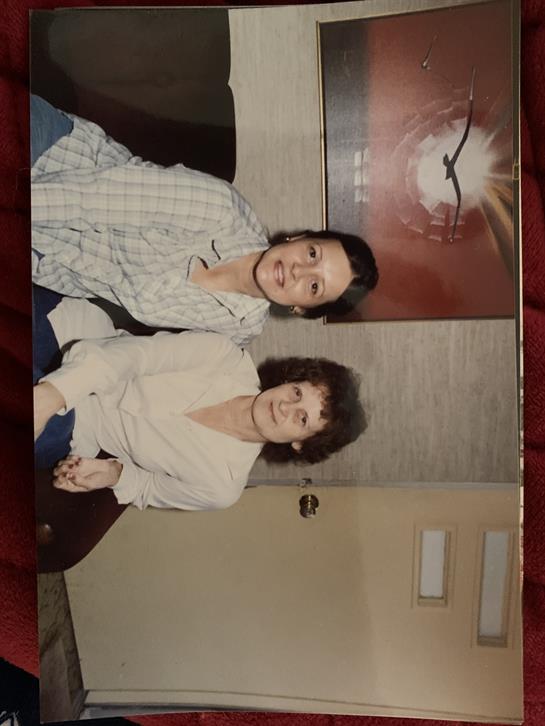 Two friends sit together on a couch, sharing smiles in a comfortable living area.