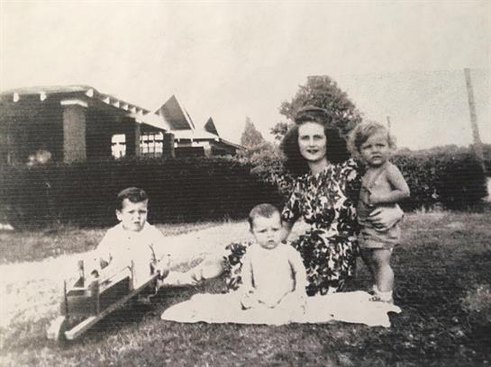 A woman and three young children are playing together on a lawn in a peaceful garden.