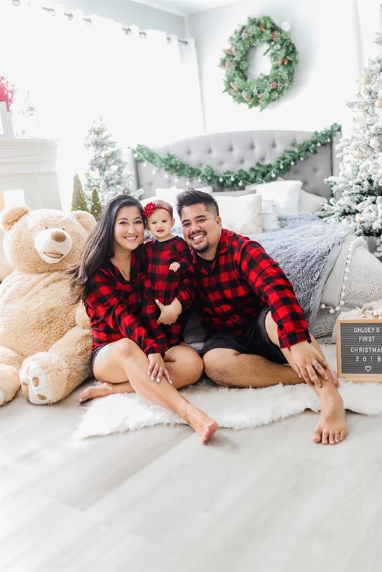 Family poses joyfully in holiday attire surrounded by festive decorations and a teddy bear.