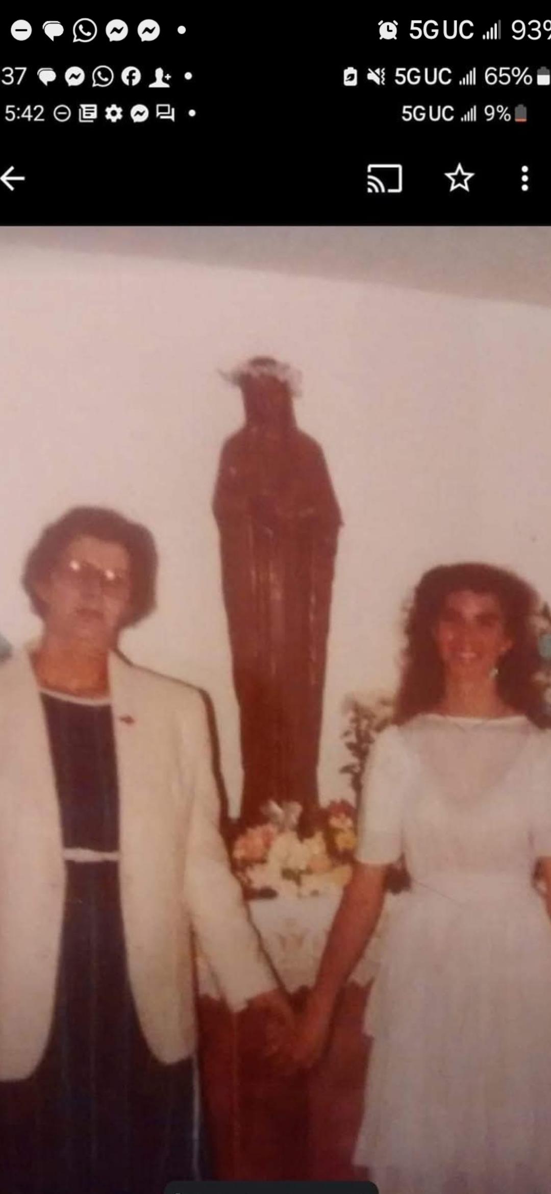 Two individuals stand hand in hand before a religious statue, radiating joy and celebration.