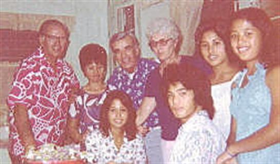 A lively family gathering shows multiple generations in vibrant outfits, smiling together.