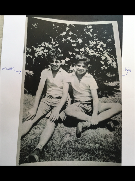 Two young boys enjoy a sunny day in a garden, posing happily while seated on the grass.