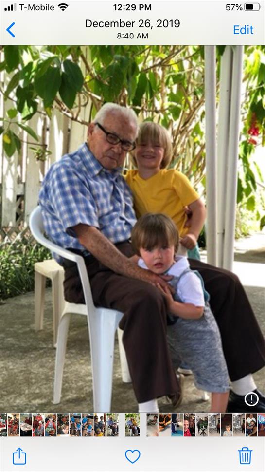 Elderly man relaxes on a chair with two smiling children in a vibrant garden.
