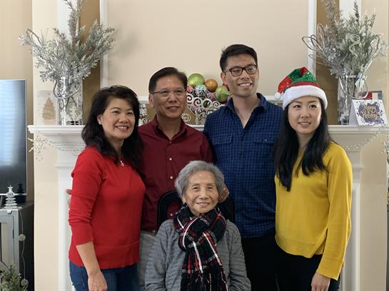 Family members pose together in a living room decorated for the holiday season, smiling warmly.