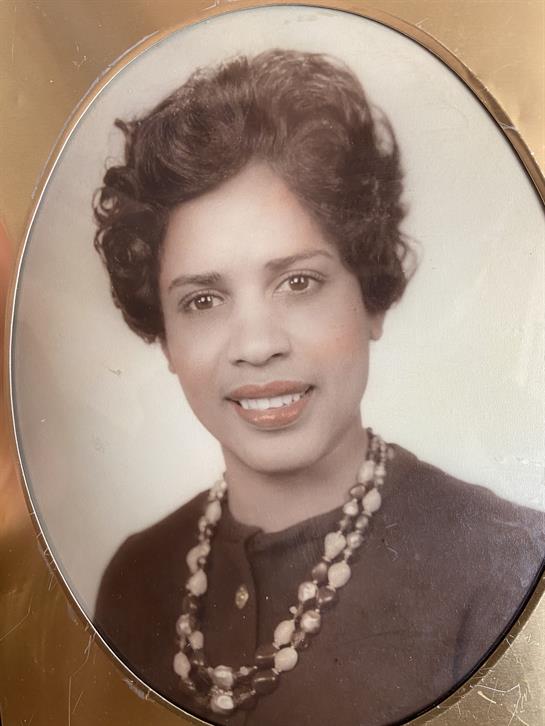 A woman with curly hair and a necklace smiles warmly, surrounded by a vintage frame.