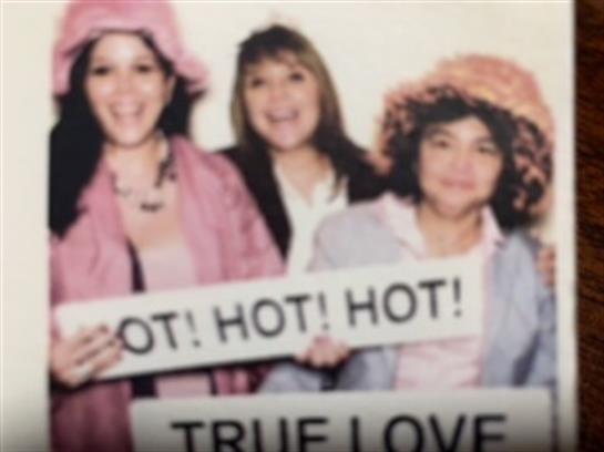 Three women hold signs expressing excitement while wearing fun hats and smiling broadly.