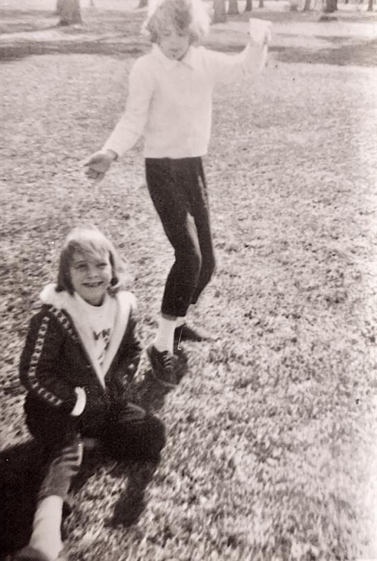 Two kids play on a grassy field, enjoying a fun afternoon under clear skies.