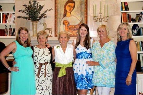 Women of various ages smile and pose together in a decorated living room during a celebration.