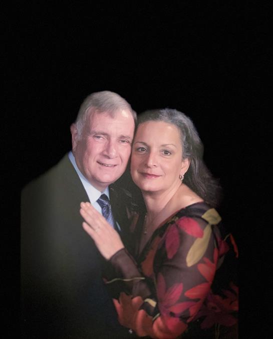 A couple in formal attire stands close, smiling warmly for a special occasion.