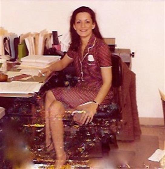 Woman in a red dress sitting at a cluttered desk, organizing paperwork during the day.