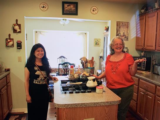 Two women stand smiling in a well-lit kitchen, cooking together and enjoying their time.