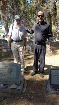 Two men stand together at a cemetery, reflecting on memories under the warm sunlight.