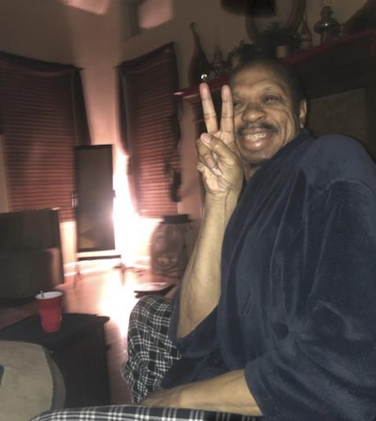 A joyful individual sits comfortably indoors, showing a peace sign while enjoying the evening.