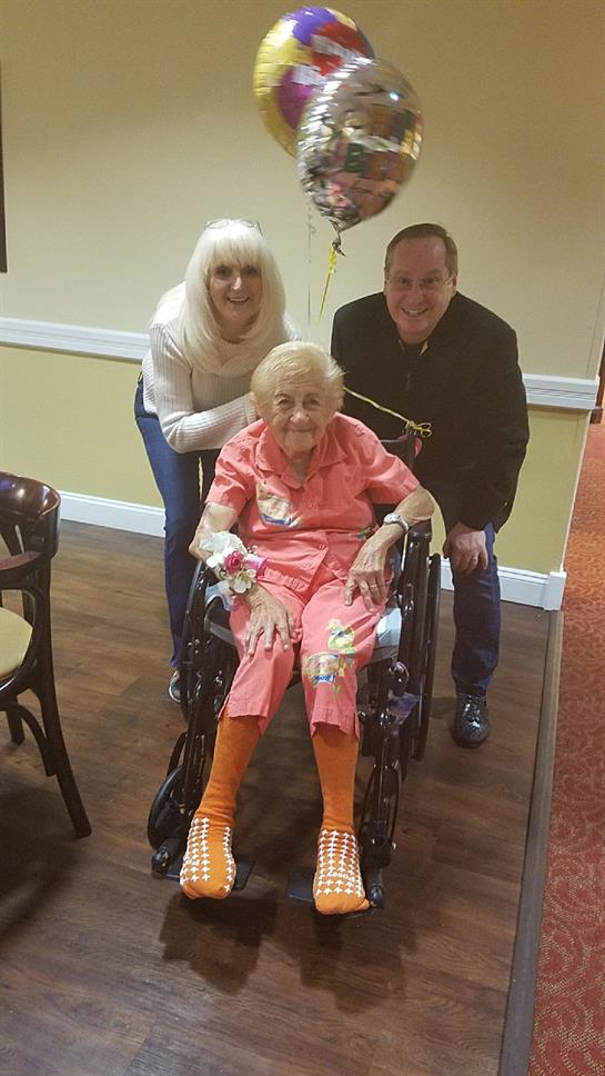 Two family members gather with a senior woman in a wheelchair, smiling and celebrating together.