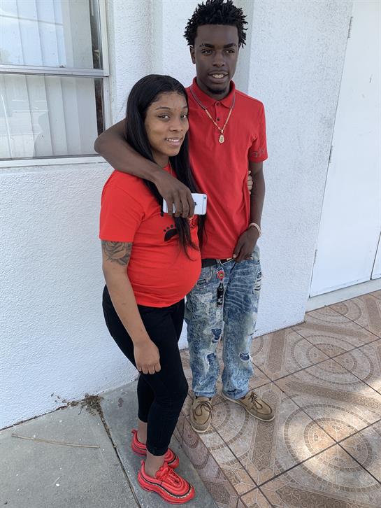 Two individuals stand side by side, dressed in red, smiling happily in a casual outdoor setting.