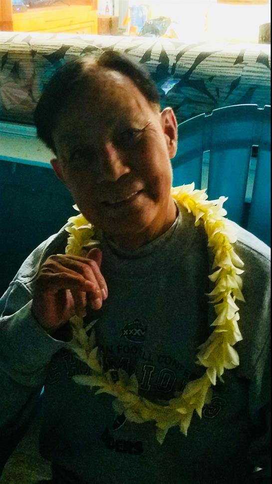 A man smiles while wearing a colorful flower lei, celebrating with friends indoors.