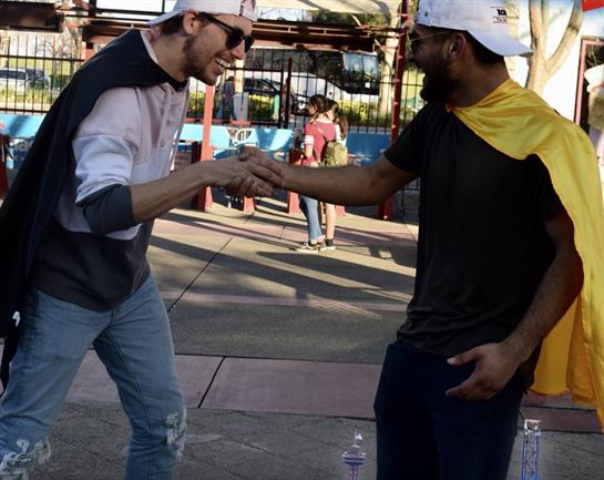 Two friends engage in a friendly handshake, surrounded by park activities and cheerful atmosphere.