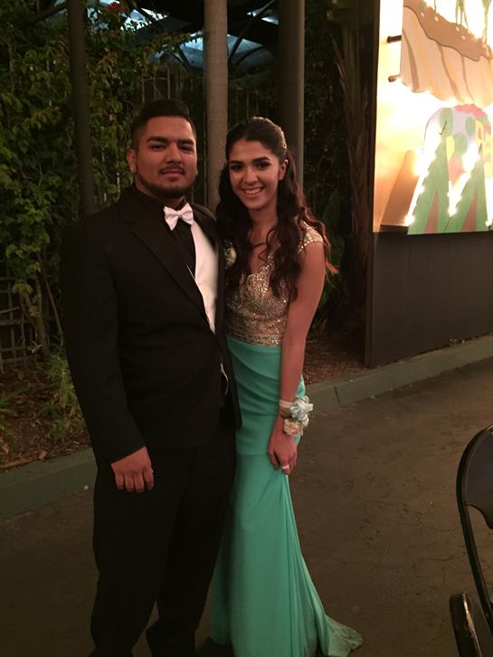 Couple smiles while wearing elegant outfits at a nighttime outdoor celebration with decorations.