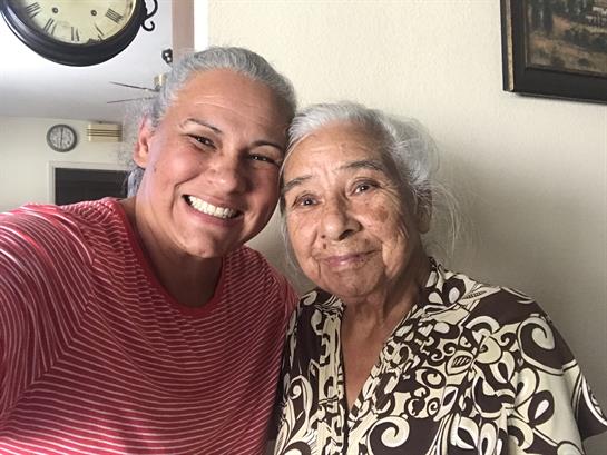 Two women share joyful smiles in a warm living room, bonding over cherished moments.